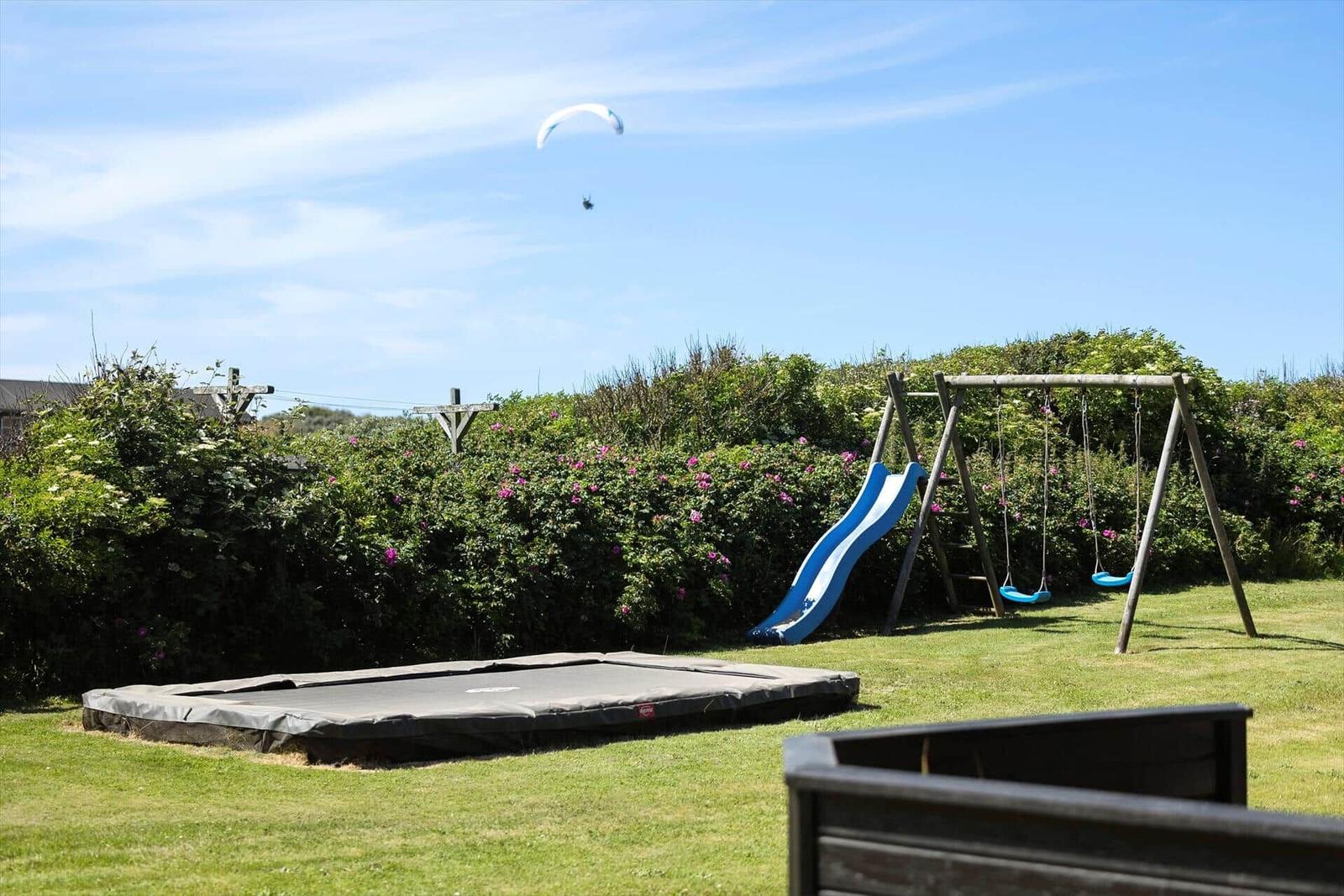 Hinterhof mit Trampolin, Rutsche und Schaukel. Im Hintergrund fliegt ein Segelflieger.