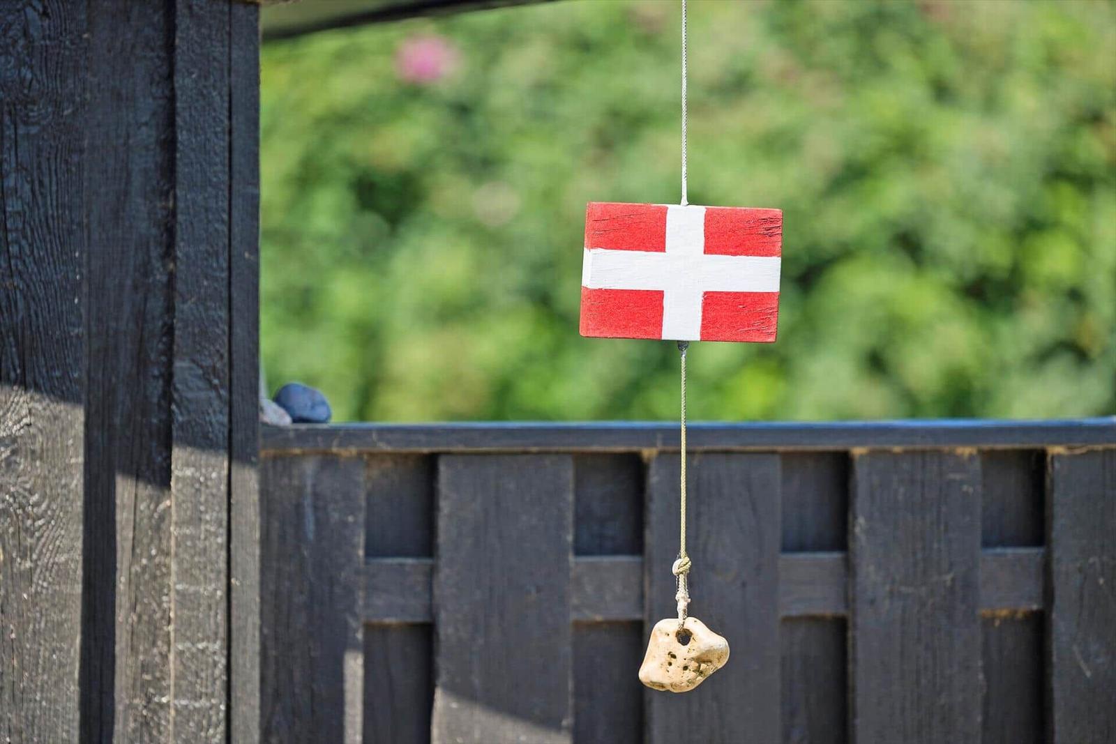 Dänische Flagge hängt an einem Seil mit Stein an einem Holzzaun.
