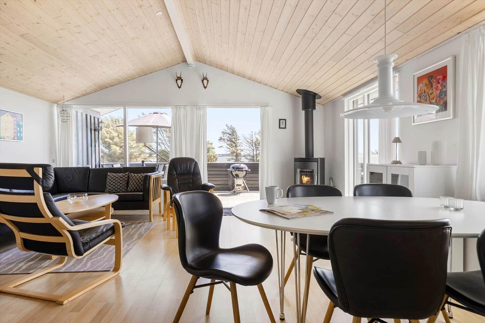 Wohn- und Essbereich mit Holzdecke, Esstisch, Sofa und Kamin.