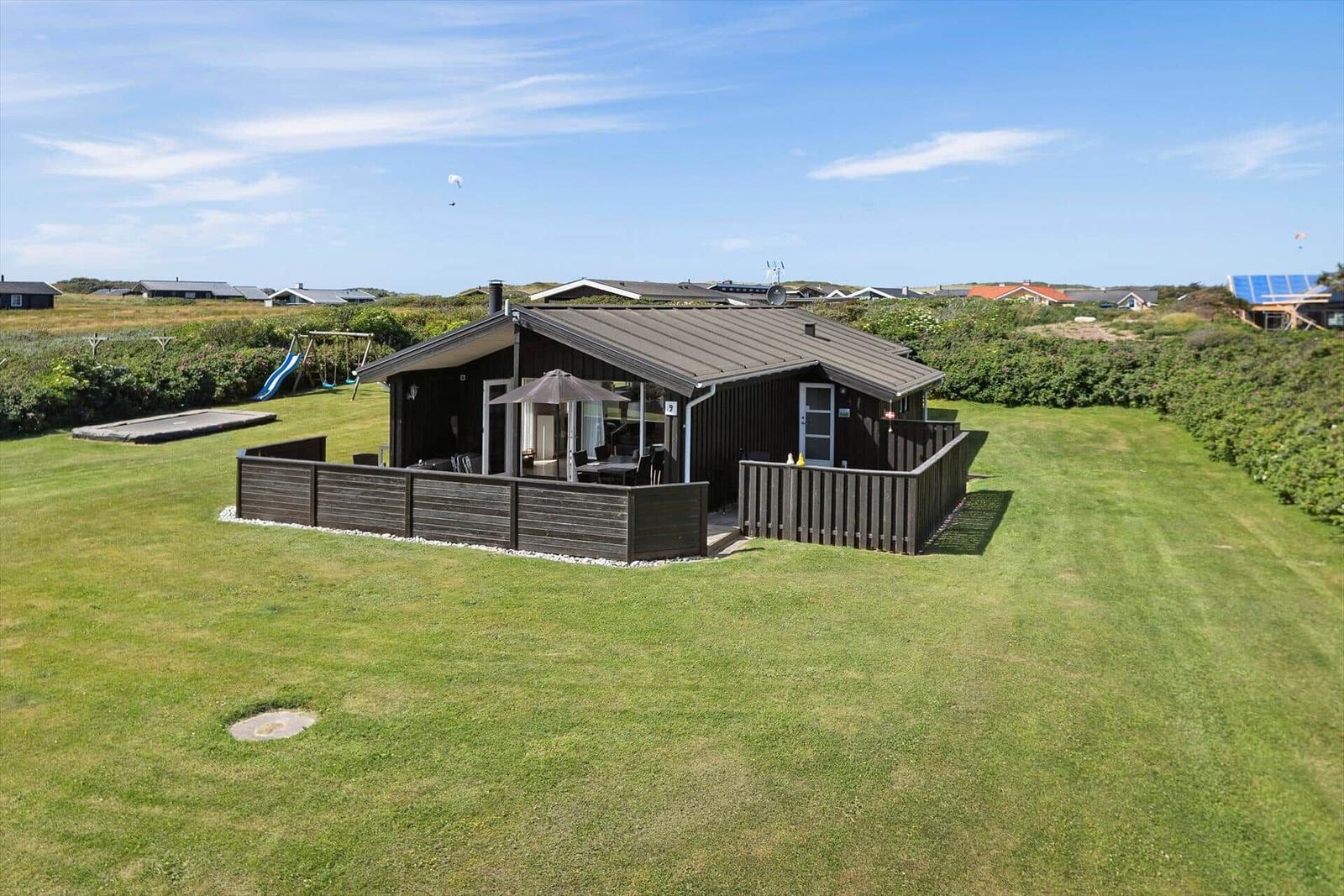 Haus mit Terrasse, Grillplatz und Spielplatz auf grünem Grundstück.