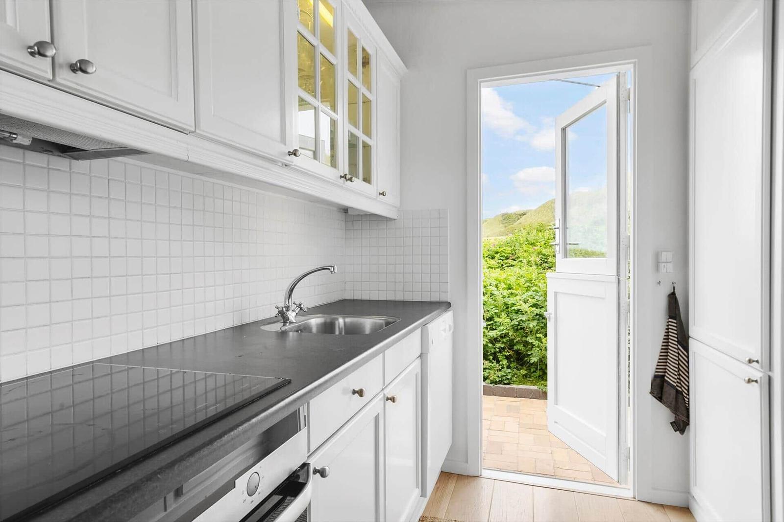 Kitchen with white cabinetry, stainless steel sink, and view of green outdoor area.