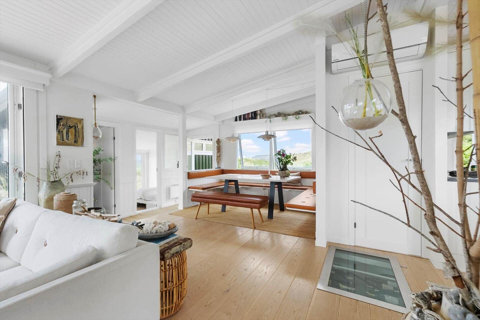 Living and dining area with white furniture and wooden floor. Windows with view of landscape.