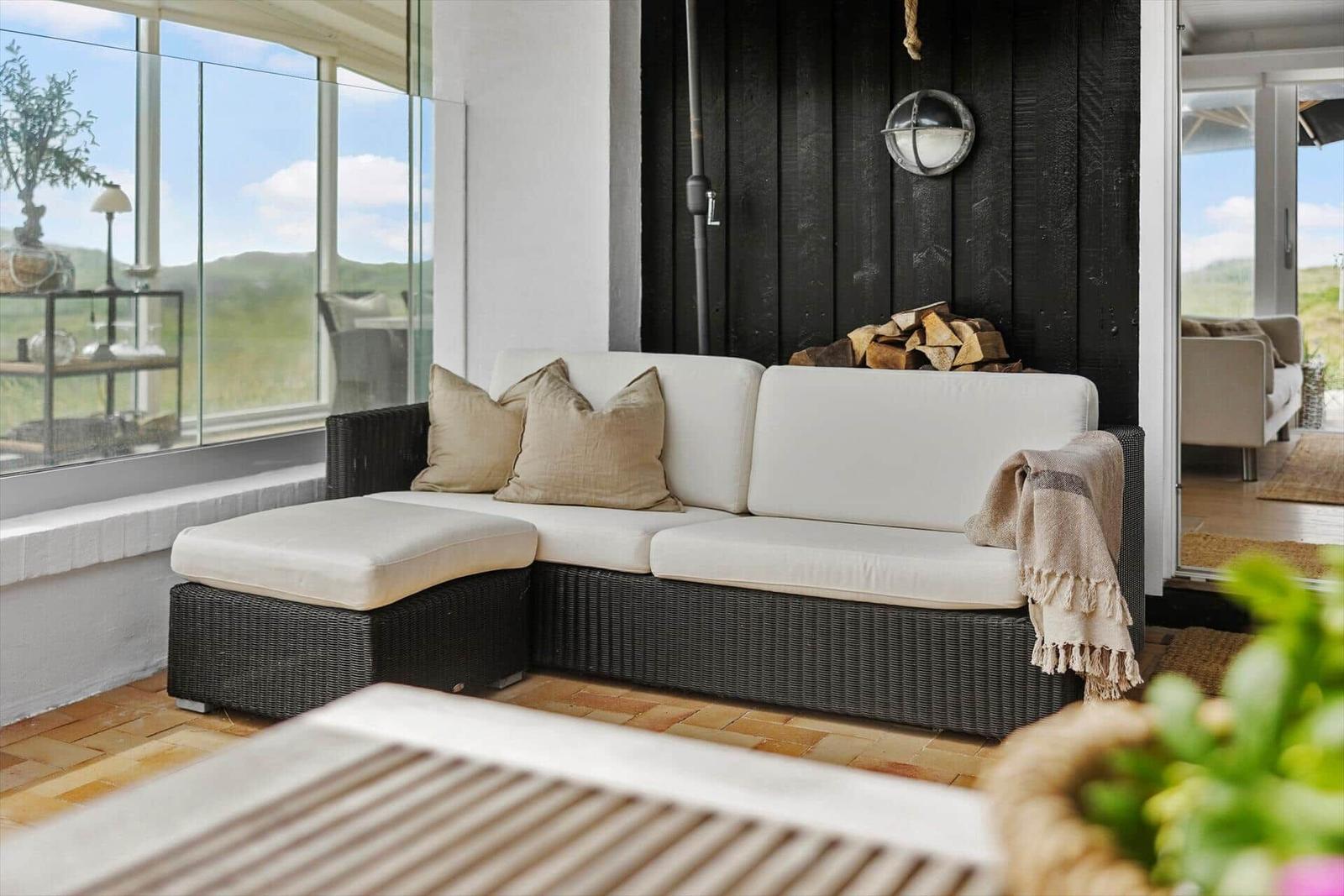 Terrace with sofa, cushions, and woodpile against black wall.