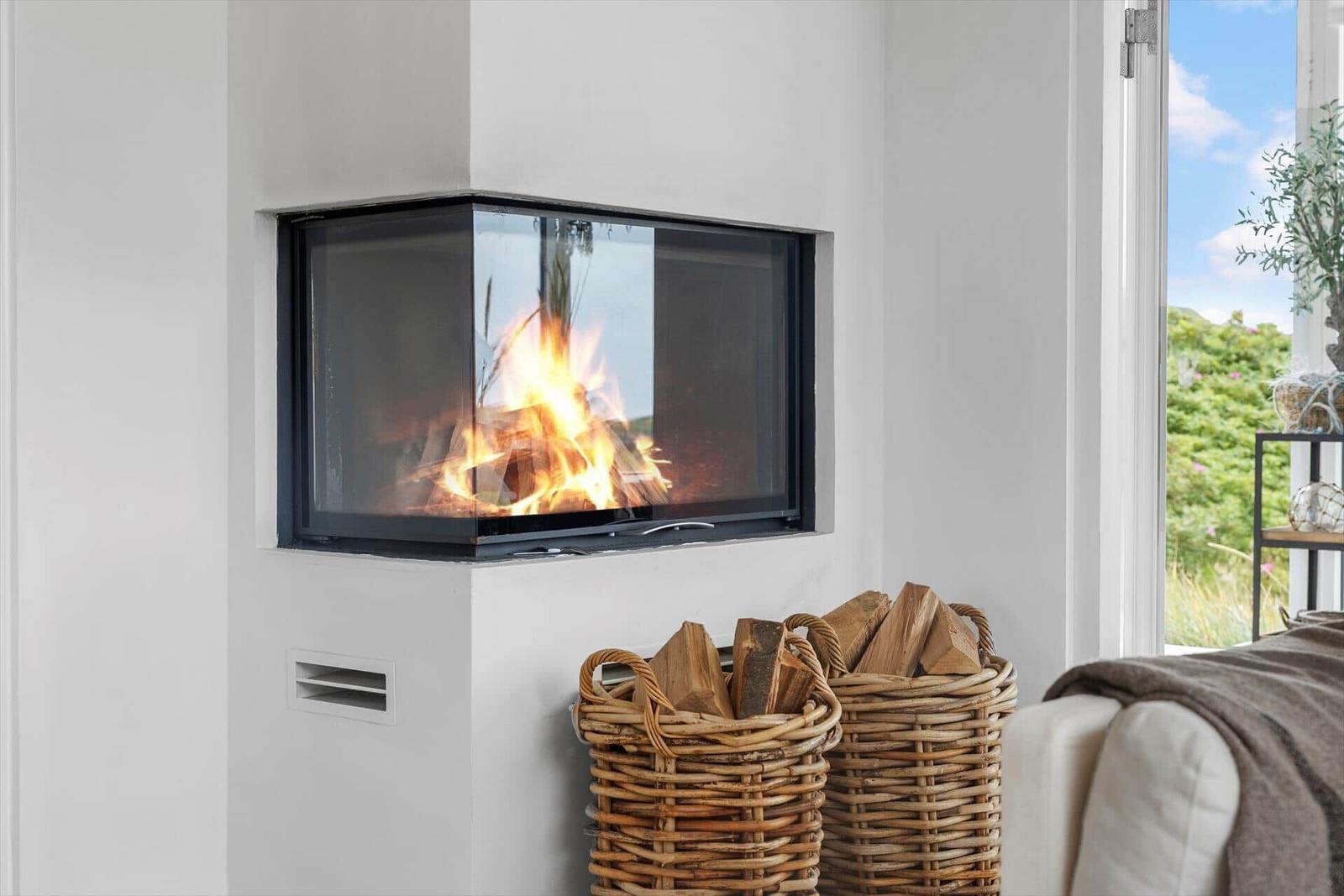 A fireplace with burning wood in a white room. Firewood in baskets stands beside it.