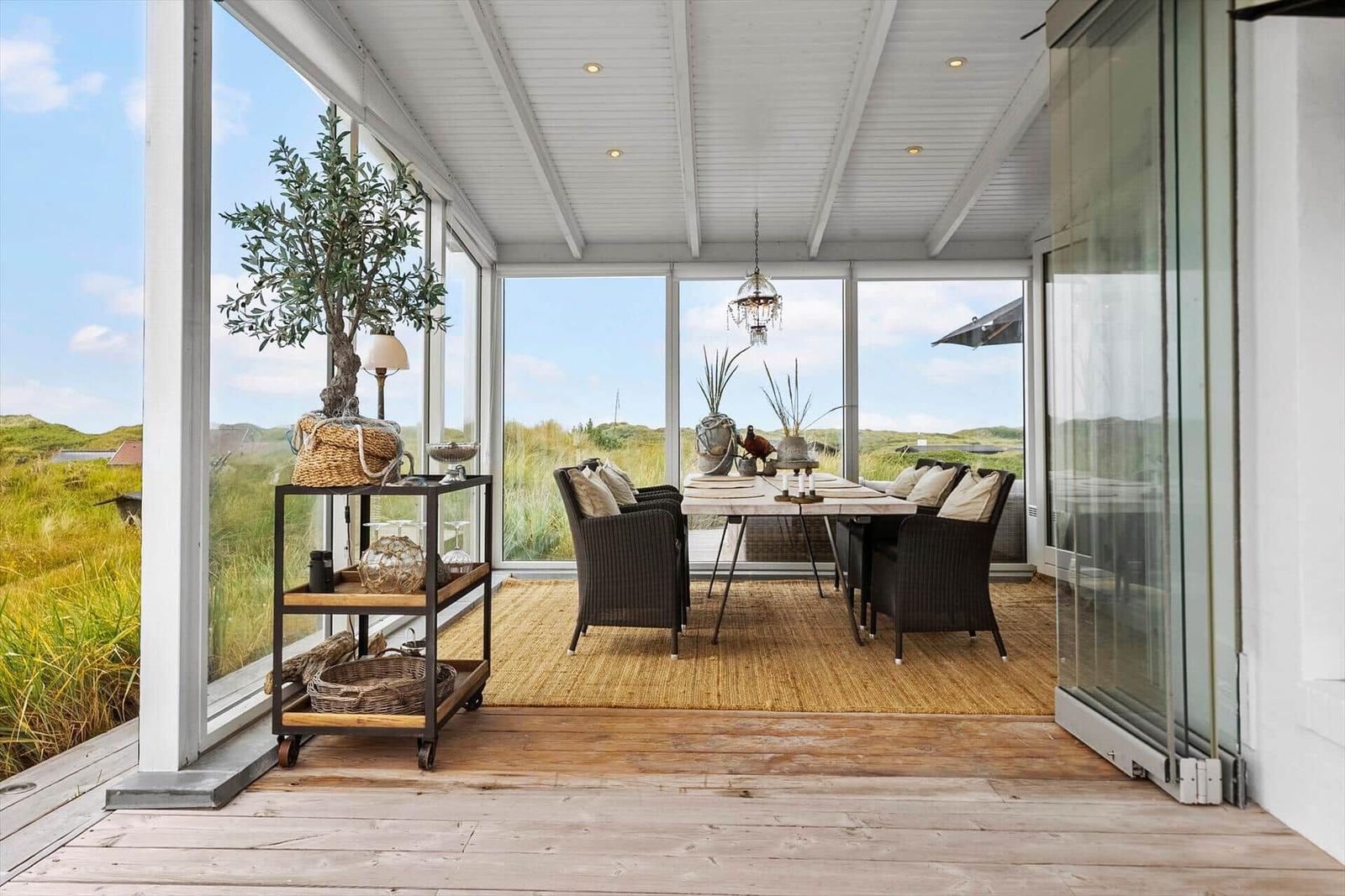 Glass veranda with dining table, chairs, and view of dunes.