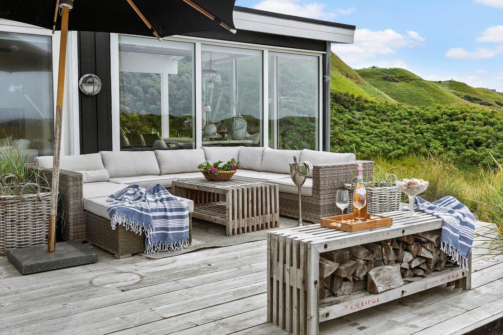 Terrace with seating, table, and firewood bench. Background: green hills.