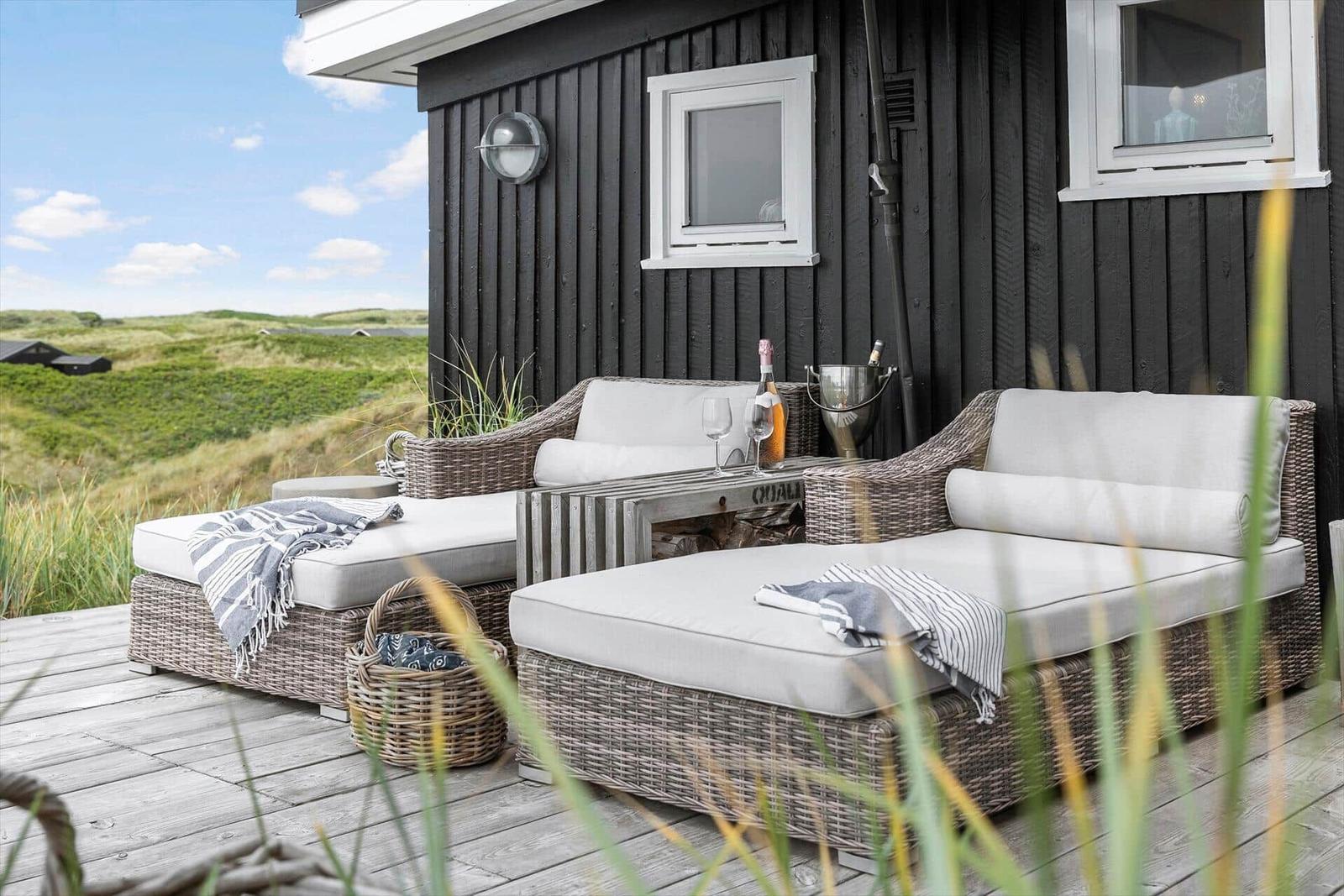 Terrace with wicker furniture, bottle and glasses. View of green dunes.