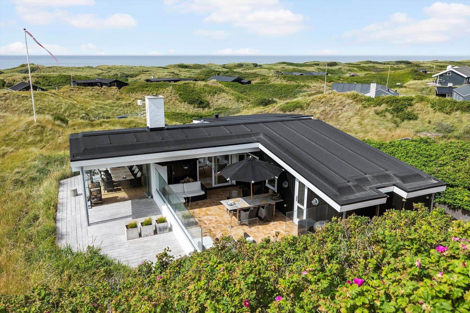 Modern villa with terrace and sea view between green dunes.