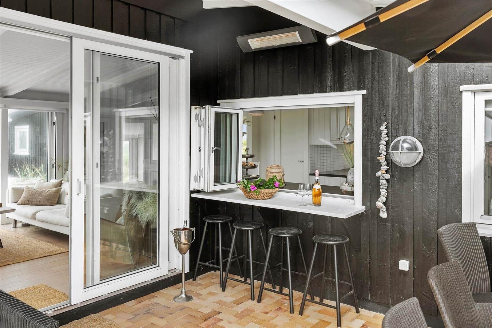 Terrace with bar, stools, and view into house. Black wood walls and wooden floor.