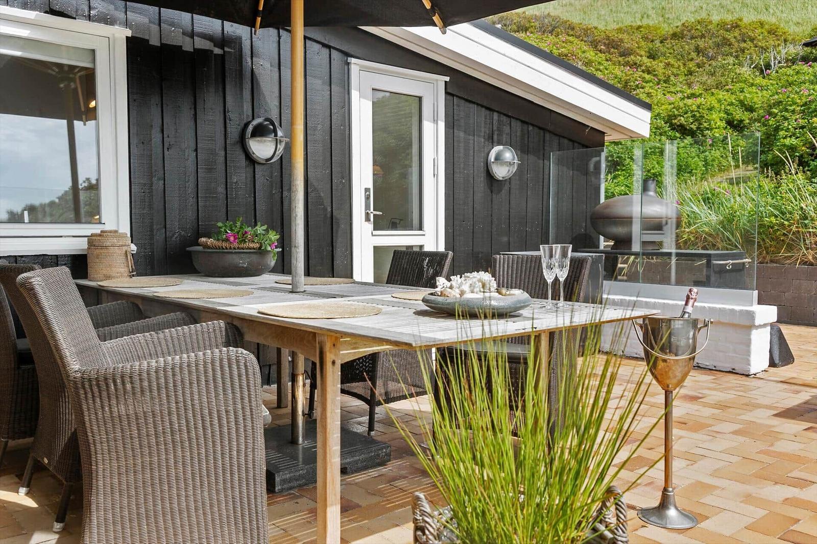 Terrace with table, chairs, and grill. Background: green landscape.