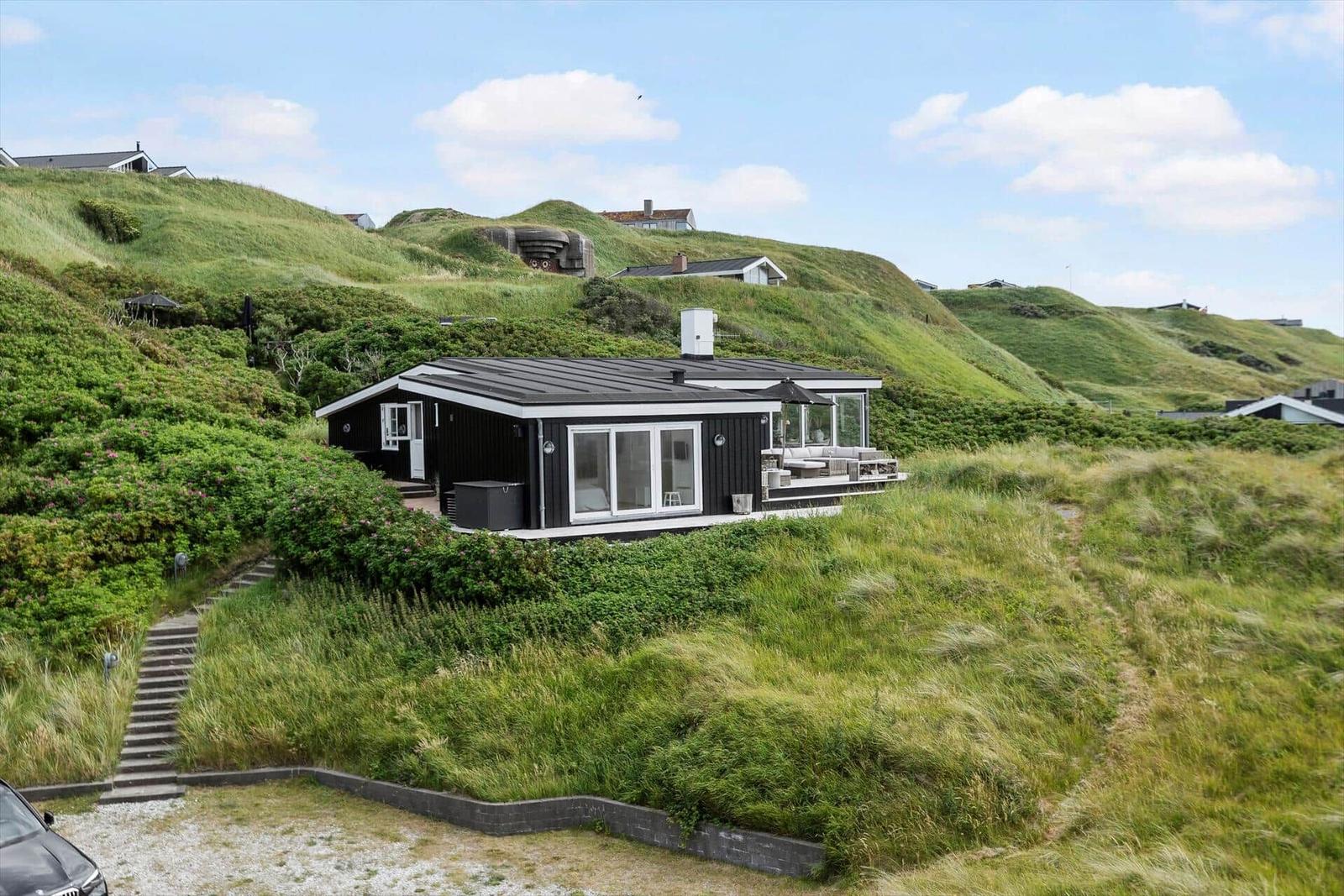 Black house with terrace on green dune landscape