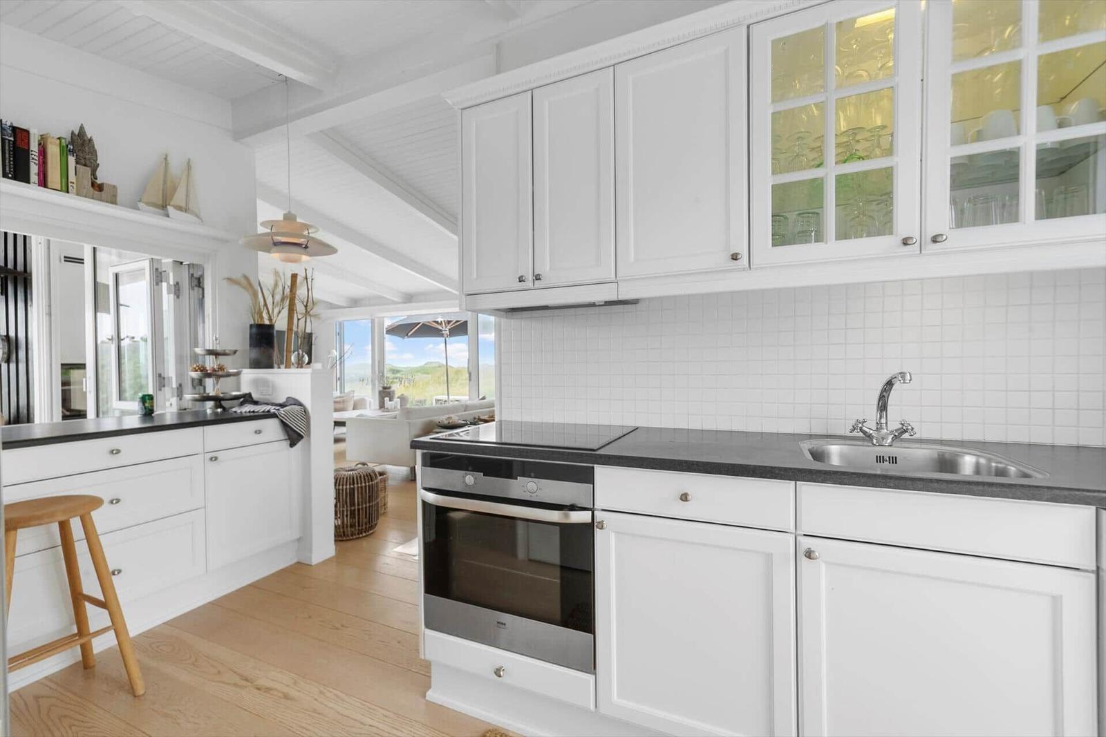 Kitchen with white cabinets, stainless steel sink, and view into living area.