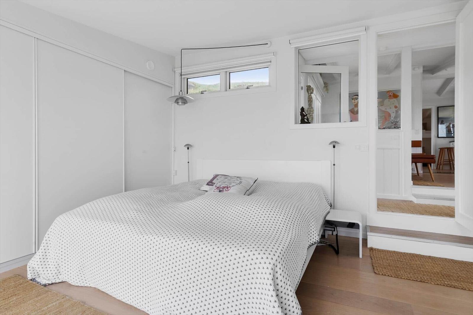 Bedroom with bed, closet, and window. Passage to living area with artwork.