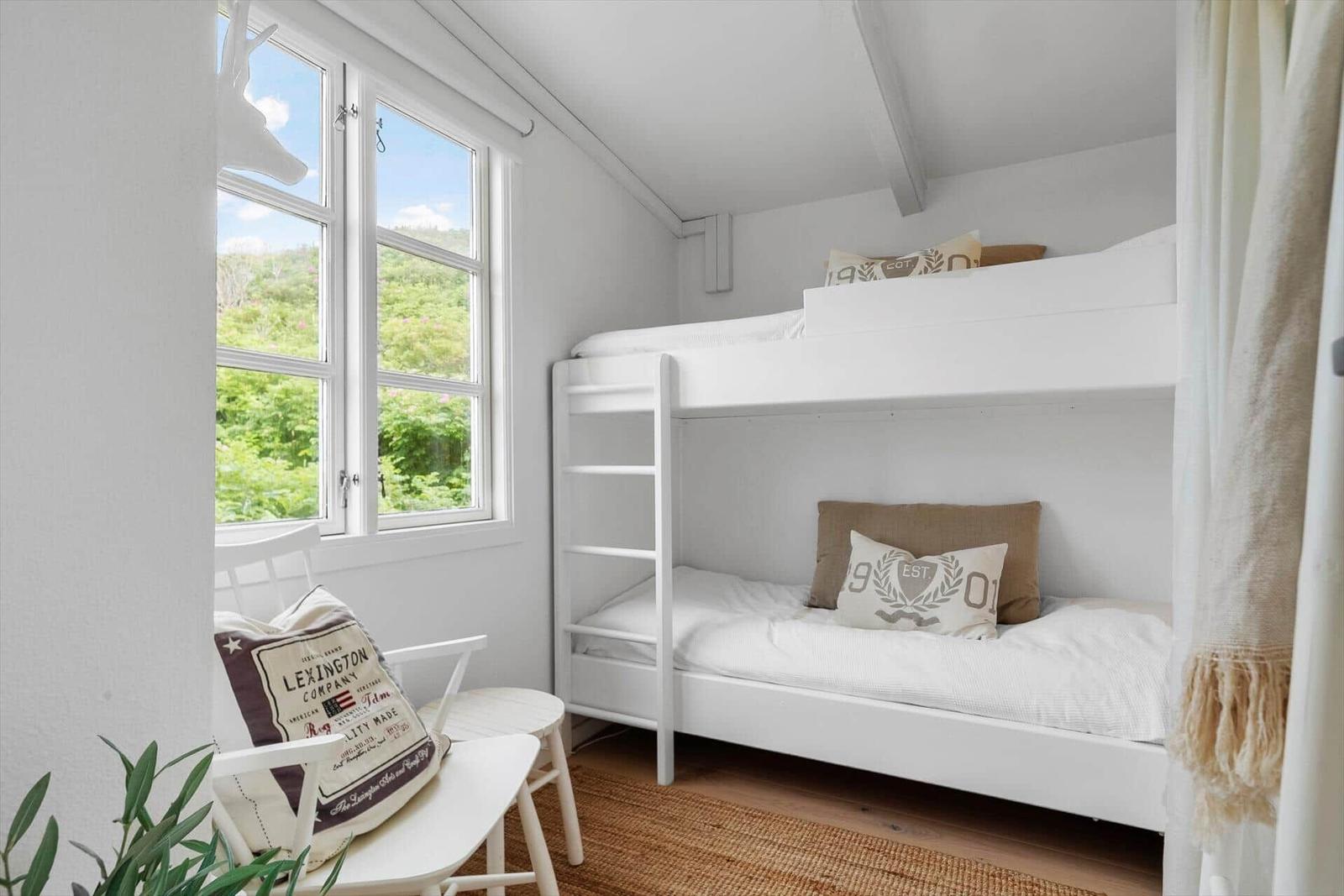 Room with bunk bed, window and chair. View of green landscape.