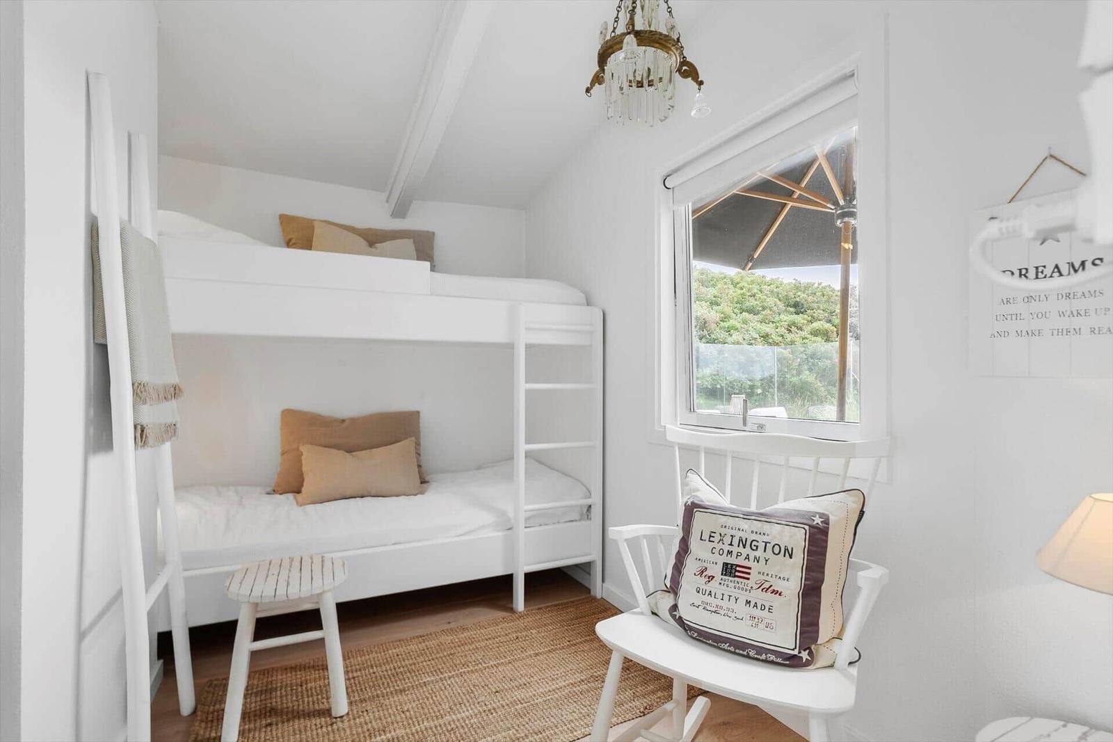 A room with bunk bed, chair, and window view of garden.