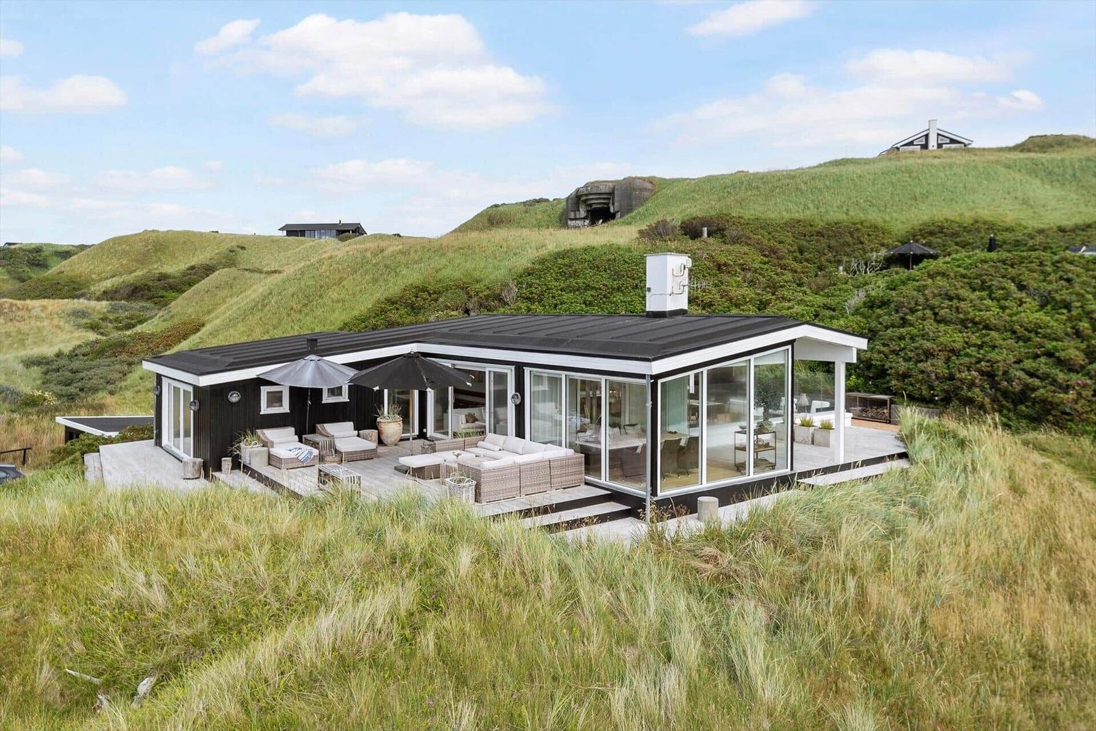 Modern villa with terrace and seating areas on green hillside.