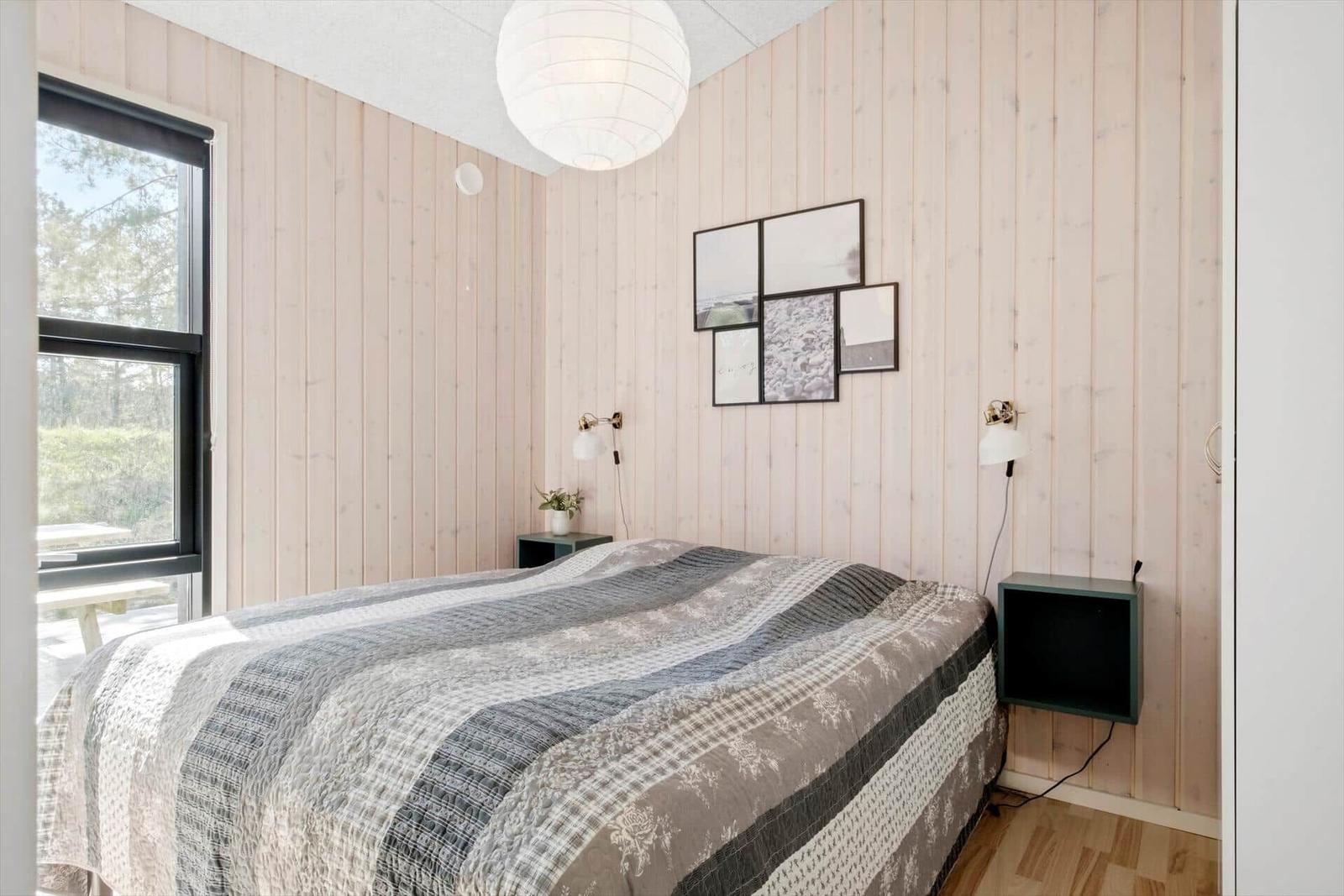 Schlafzimmer mit Bett, Wandlampen und Fenster zum Garten.