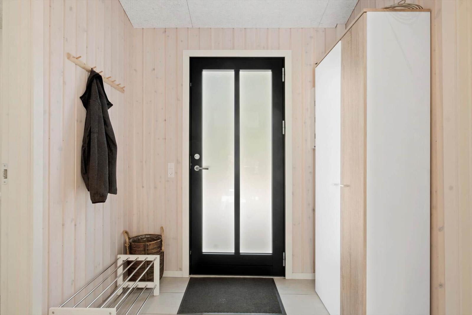Eingangsbereich mit Holzwand, Garderobe, Schrank und Tür mit Glasflächen.