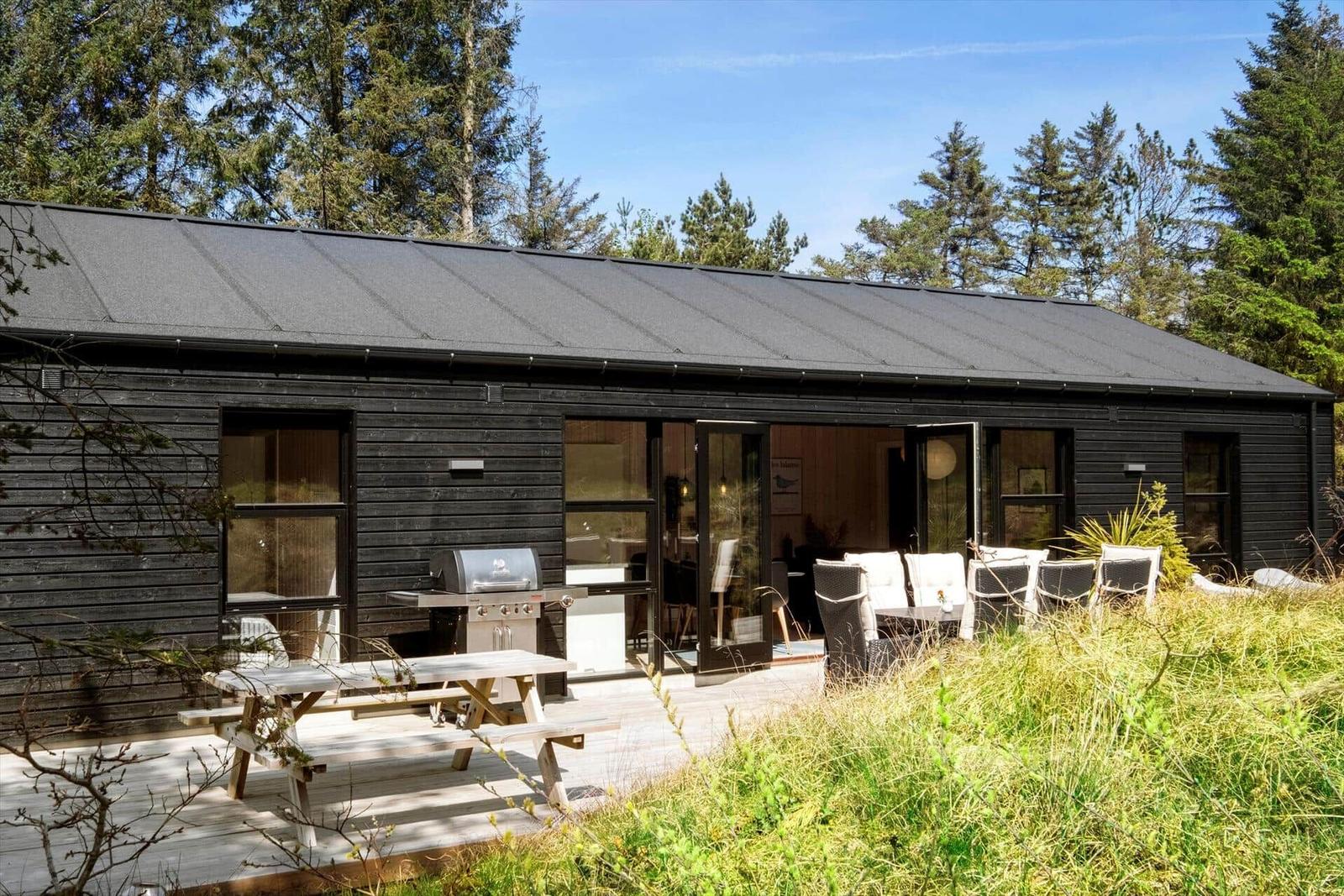 Moderne Holzhütte mit Terrasse, Grill und Gartenmöbeln in Waldnähe.