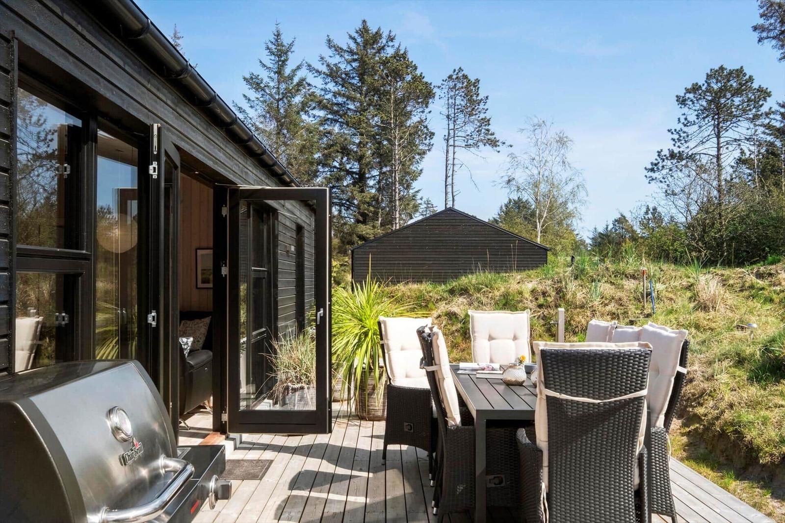 Terrasse mit Sitzgruppe und Grill, Blick auf Wald und Schuppen.