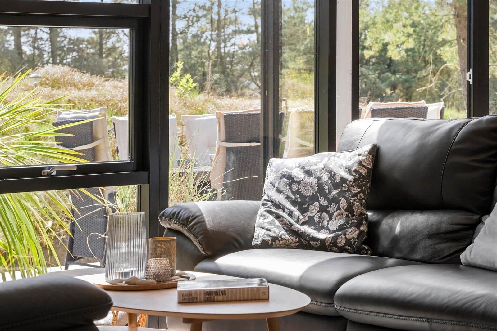 Ein schwarzes Sofa mit Kissen vor großen Fenstern mit Blick auf Gartenmöbel.