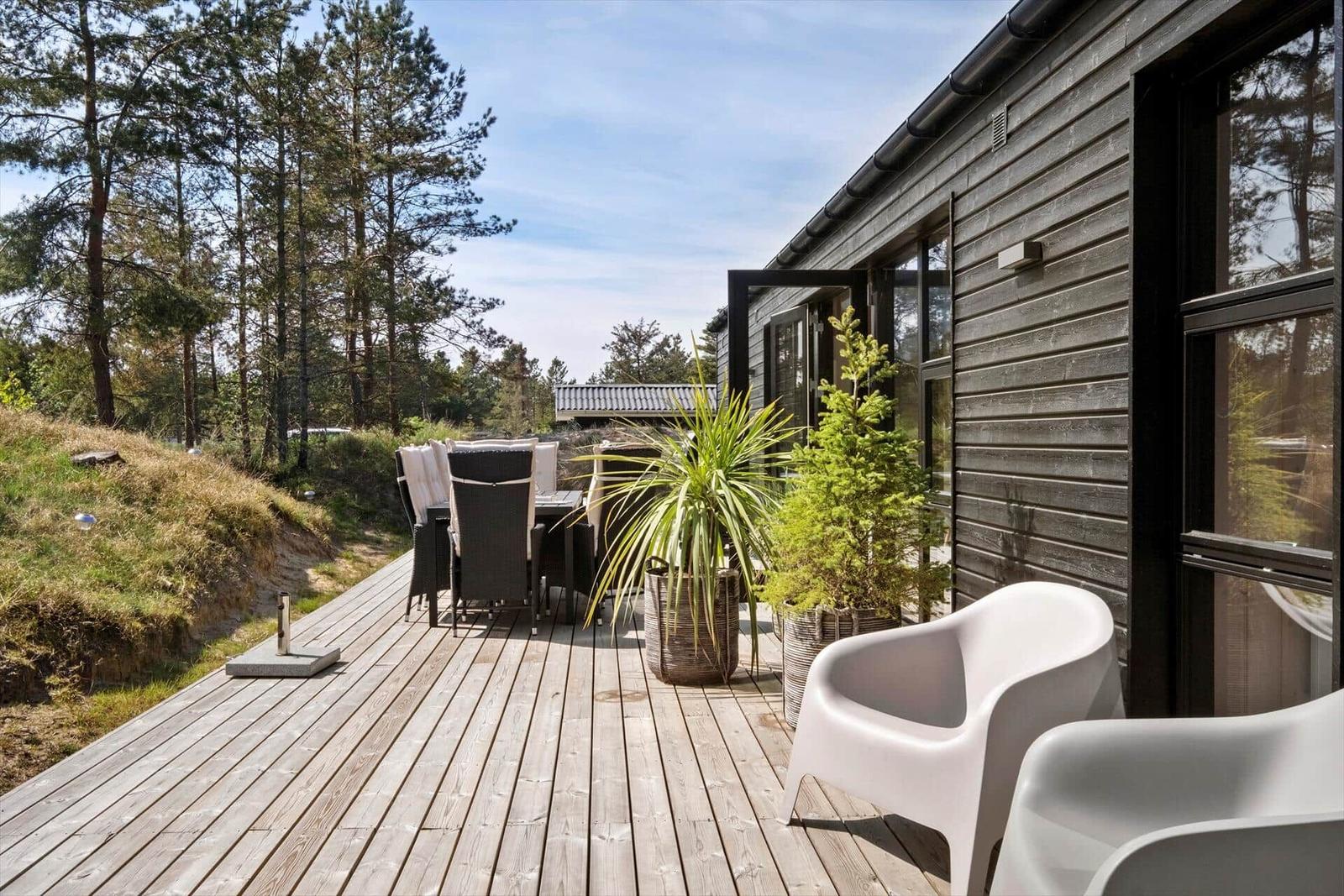 Terrasse mit Sitzgelegenheiten und Pflanzen vor einem Holzhaus.