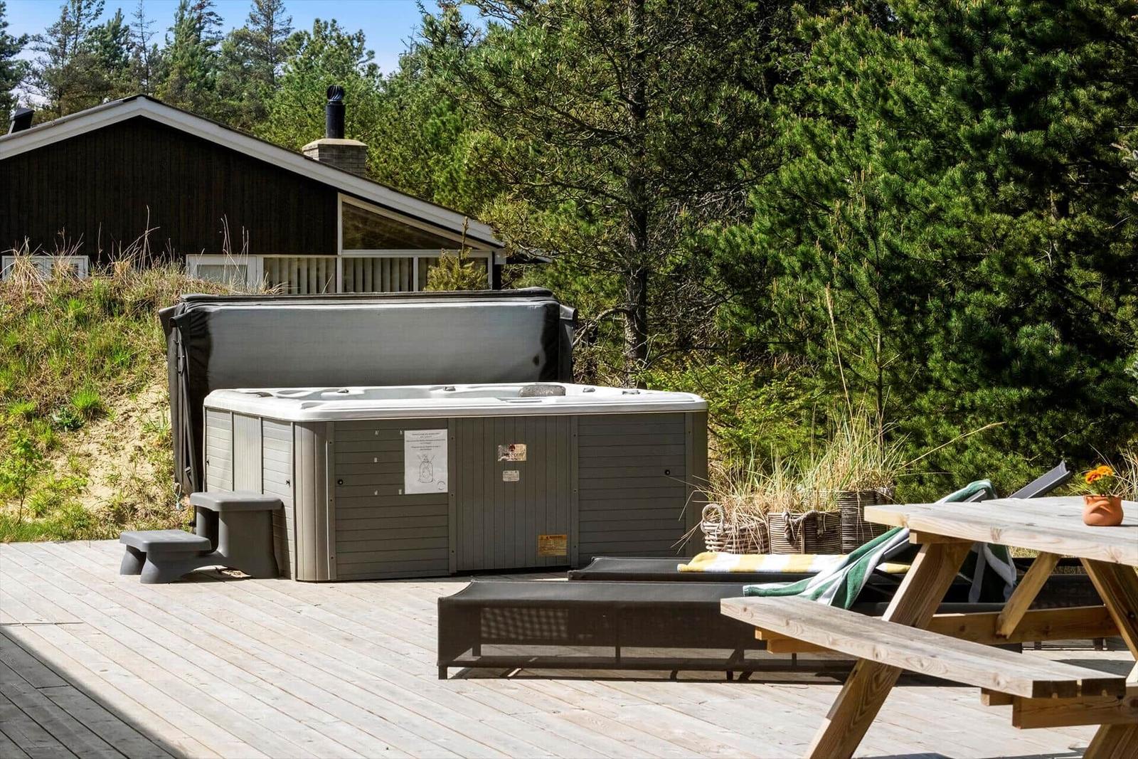 Hochwertige Außenterrasse mit Whirlpool, Picknicktisch und Liegen umgeben von Bäumen.