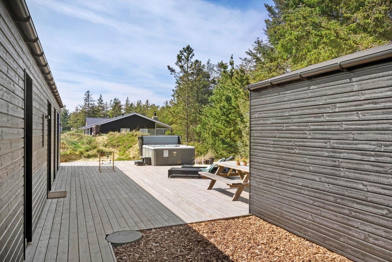 Terrasse mit Hot Tub, Picknicktisch und Grillplatz zwischen Holzwänden und Wald.