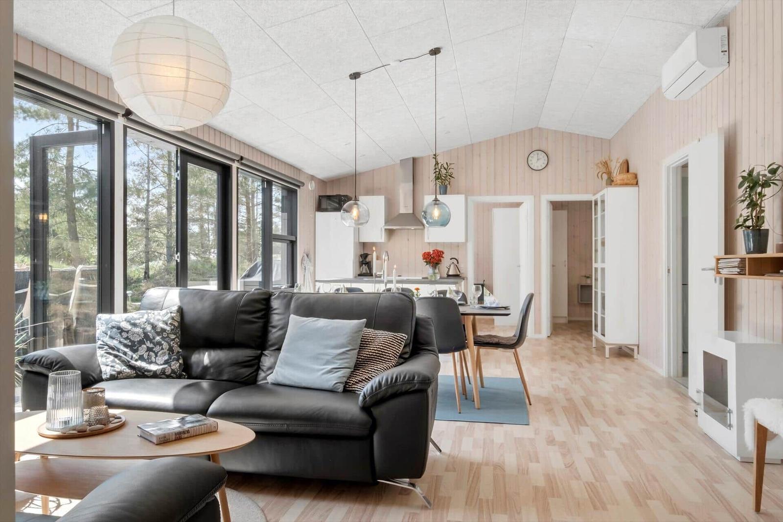 Wohnzimmer mit Sofa, Essbereich und Küche. Holzfußboden und große Fenster.