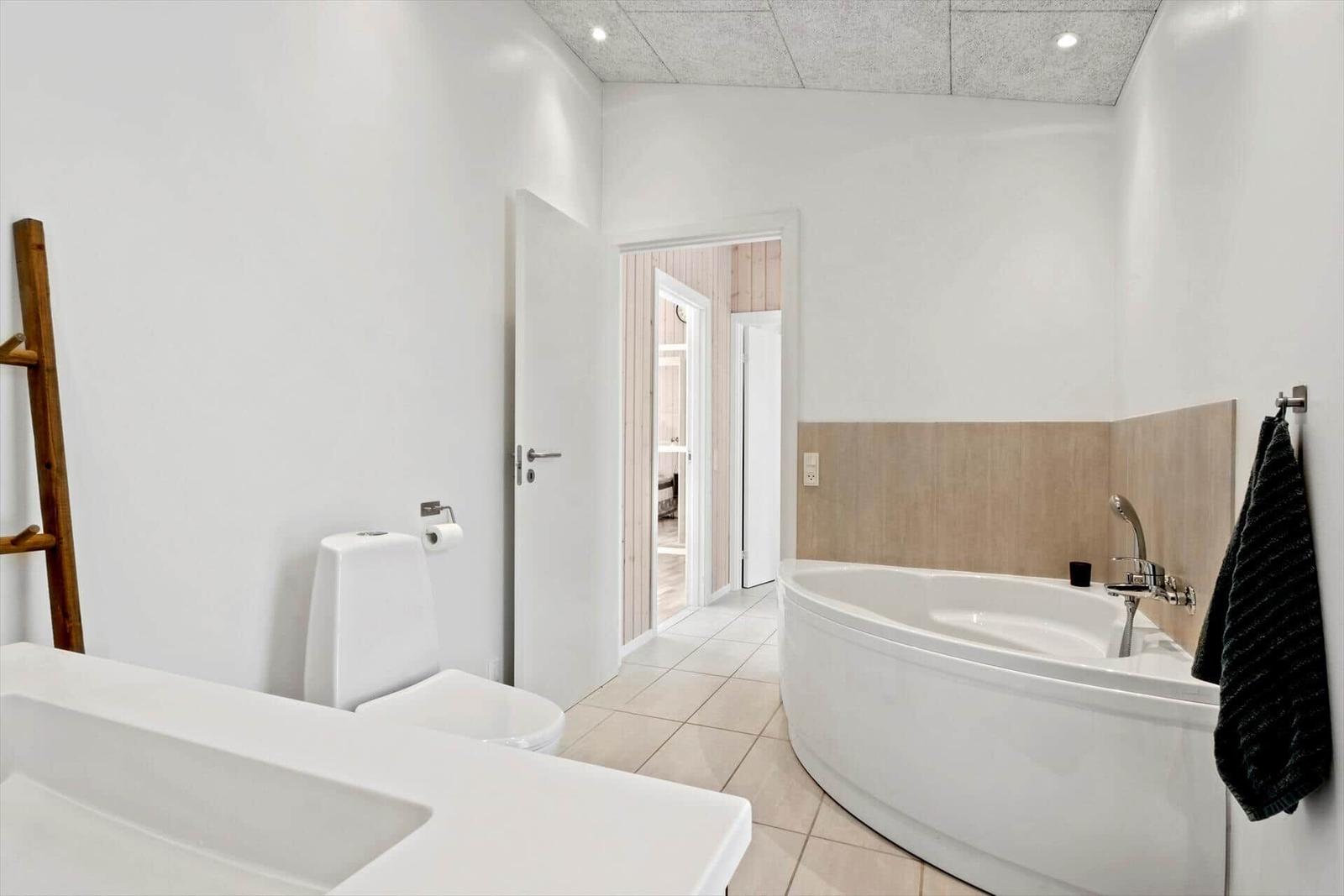 Badezimmer mit Badewanne, Toilette und Waschbecken. Holzwand im angrenzenden Raum.