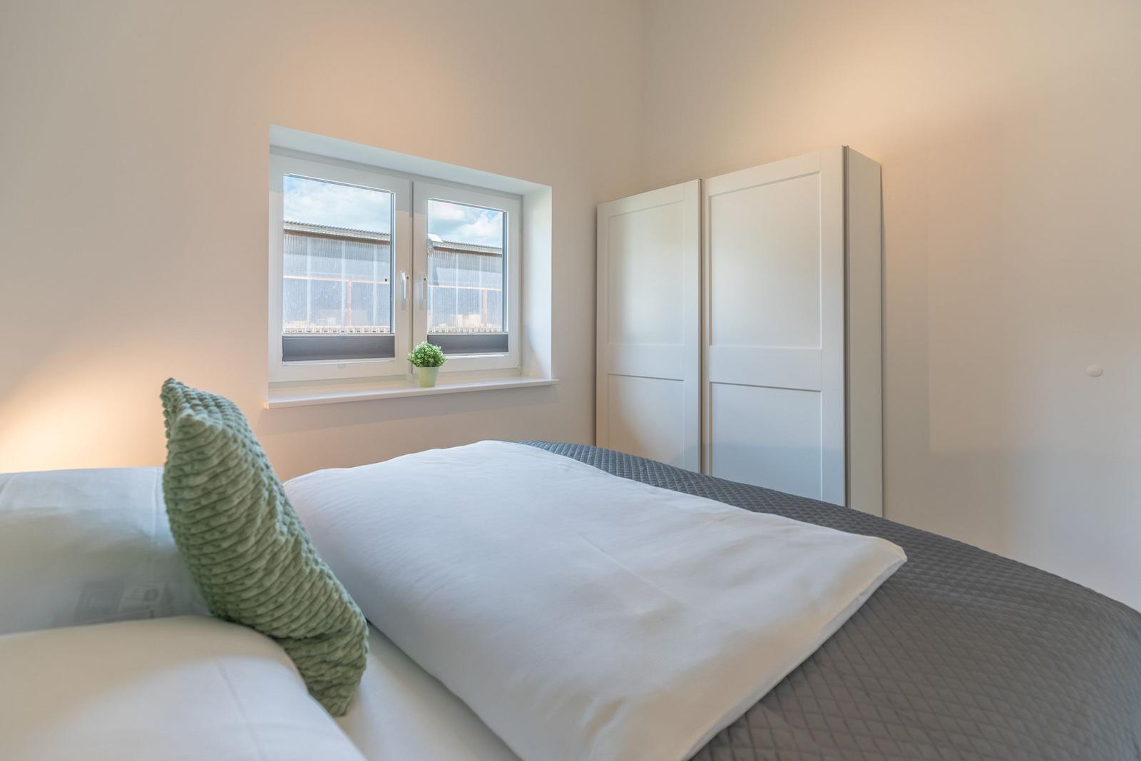 Schlafzimmer mit Bett, Kleiderschrank und Fenster.