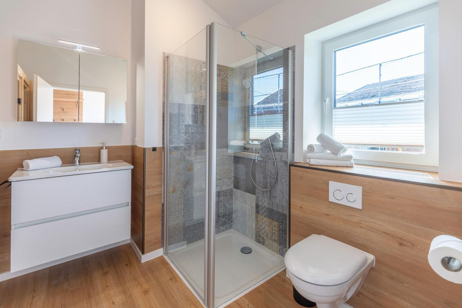 Badezimmer mit Dusche, Waschbecken und Toilette. Holz- und Steinoptik.