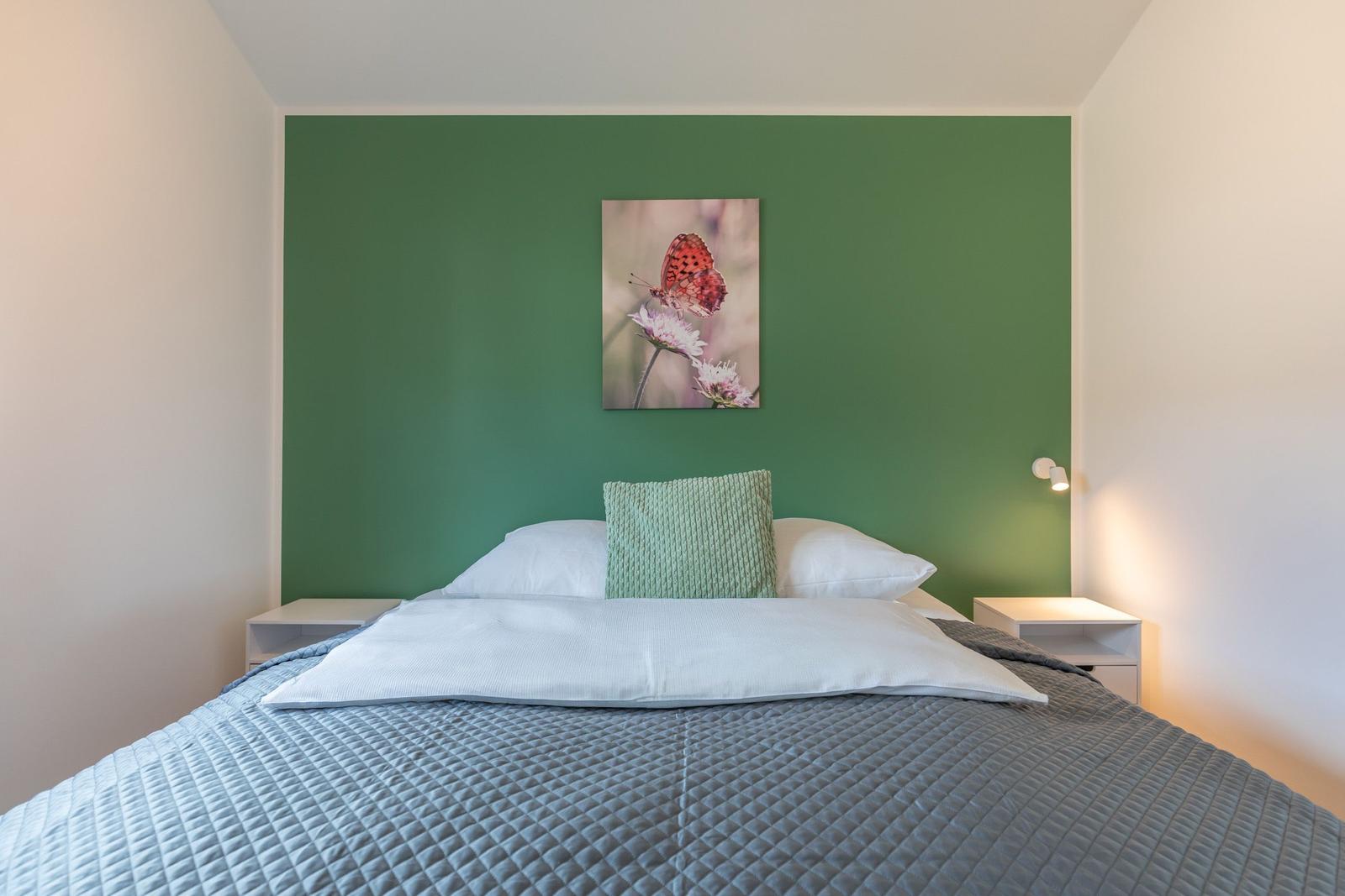 Schlafzimmer mit Bett, grüner Wand und Wandbild mit Schmetterling.