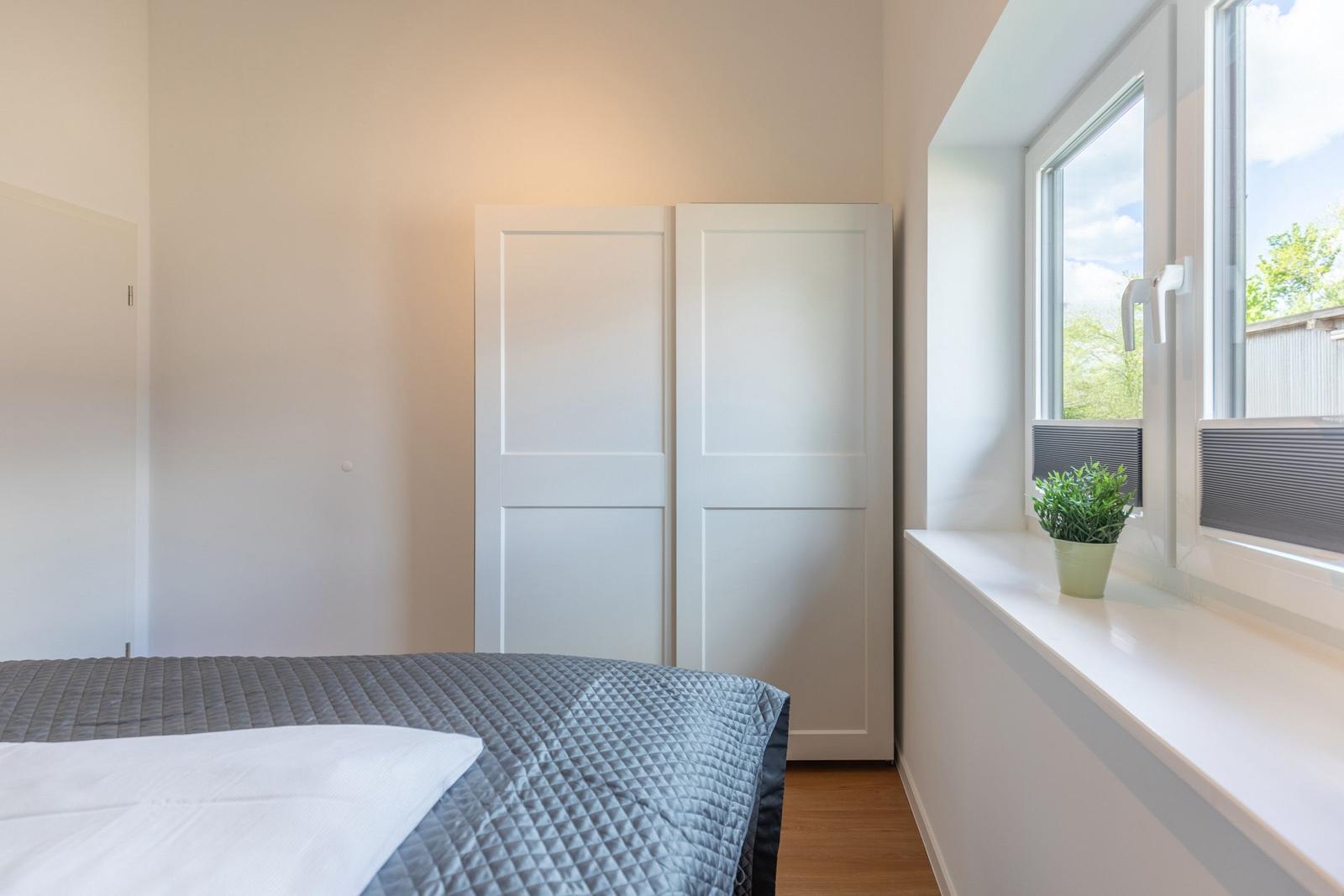 Schlafzimmer mit Bett, Kleiderschrank und Fenster mit Pflanze.
