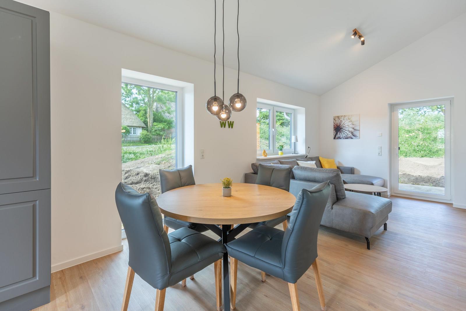 Essbereich mit runden Tisch und Stühlen. Wohnbereich mit Sofa und Fenstern.