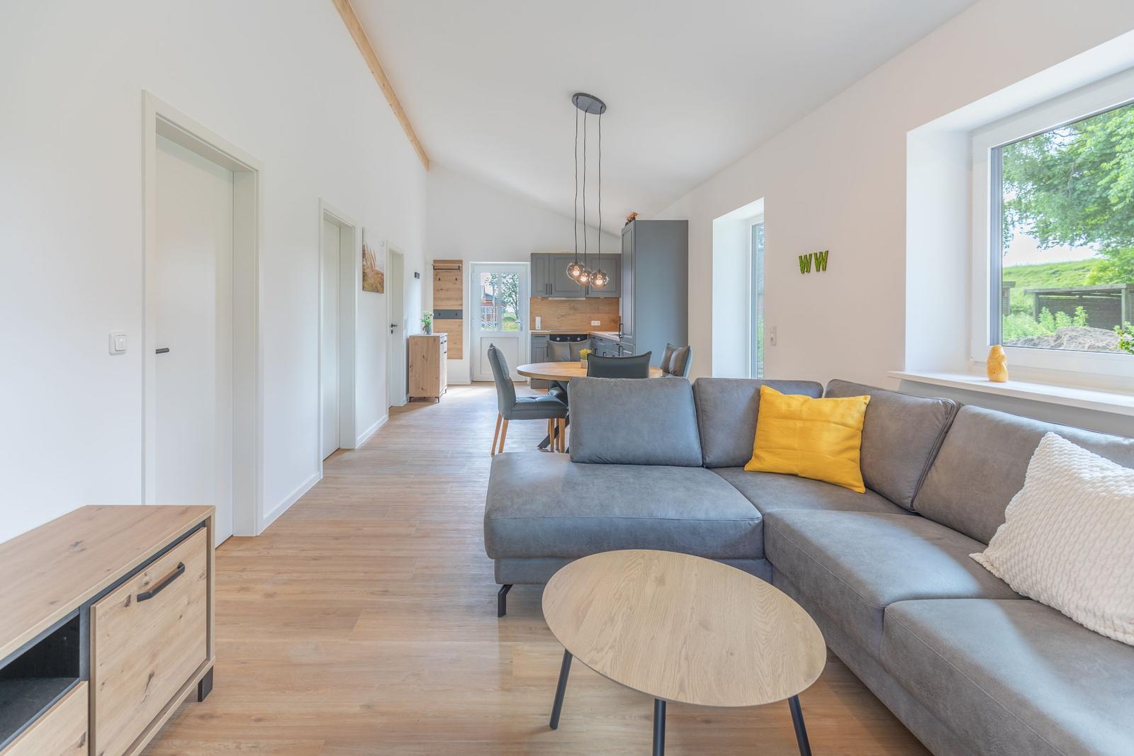 Wohn- und Essbereich mit grauem Sofa, Holzboden und großem Fenster.