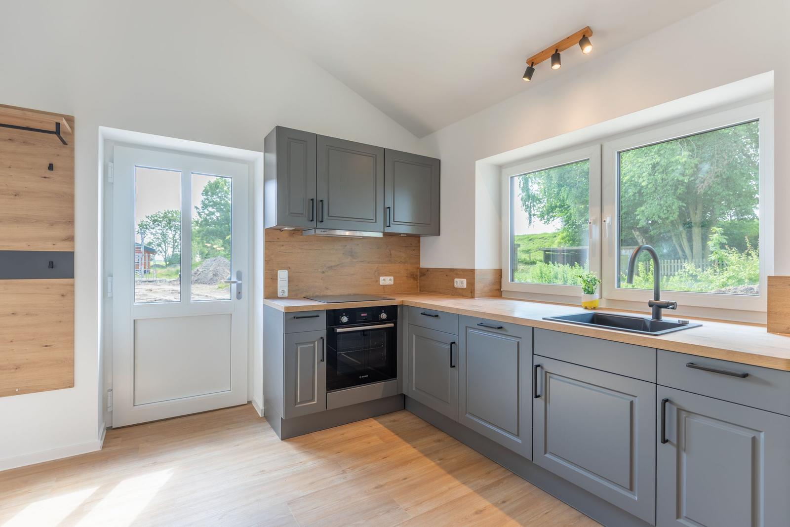 Küche mit grauen Schränken, Holzoberfläche und Blick auf grüne Landschaft.