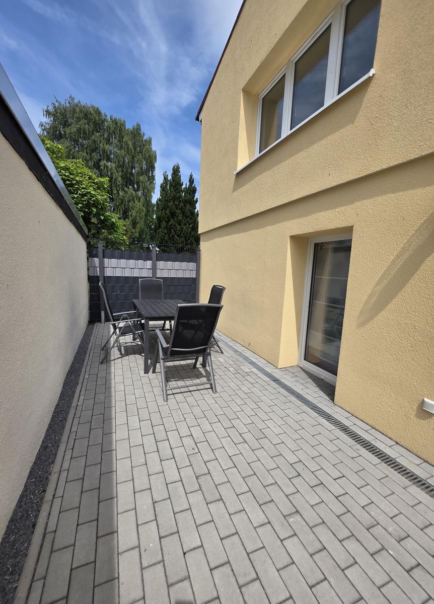 Terrasse mit Tisch und Stühlen neben gelbem Haus mit Fenstern.