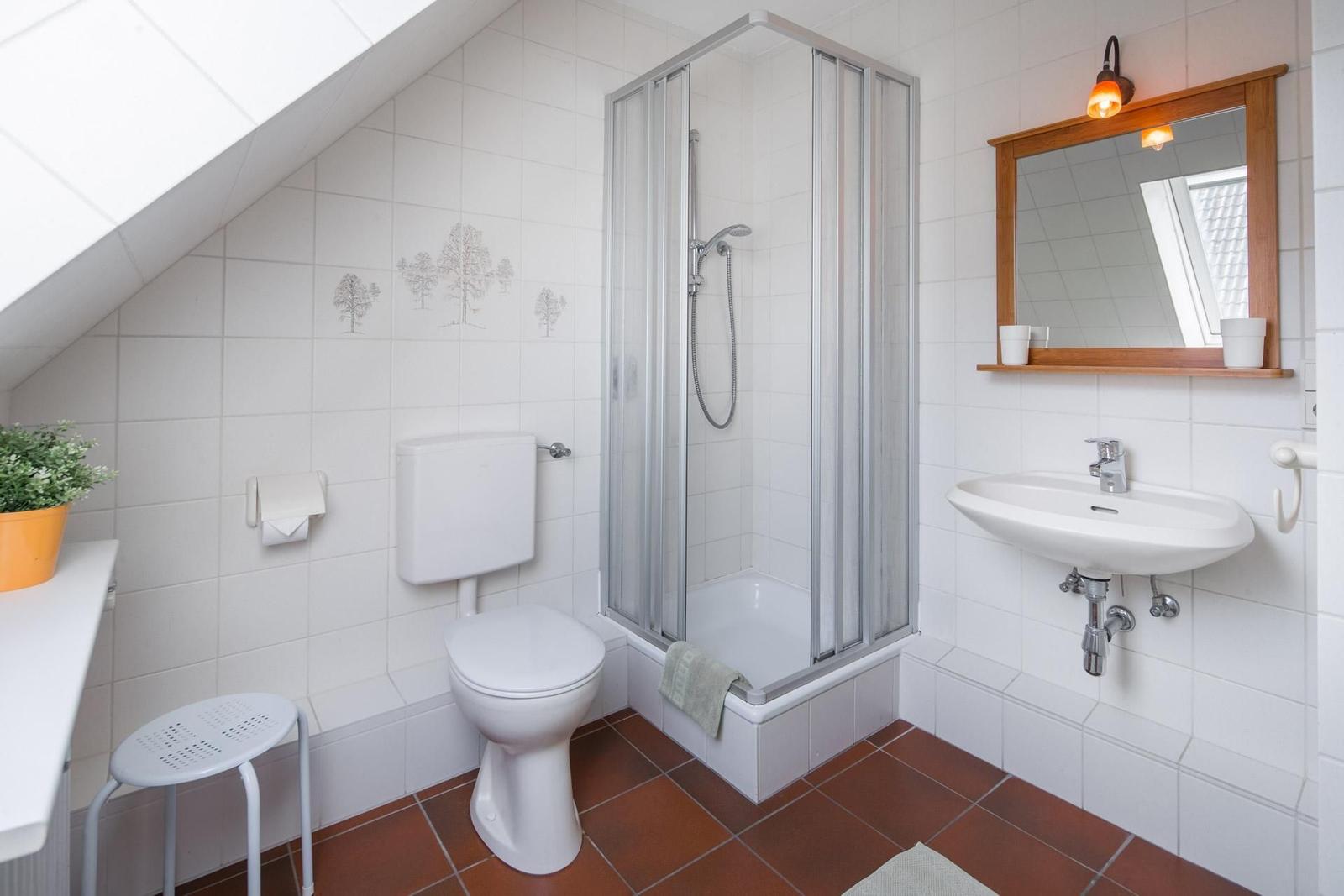 Badezimmer mit Dusche, Waschbecken und Toilette unter Dachschräge.