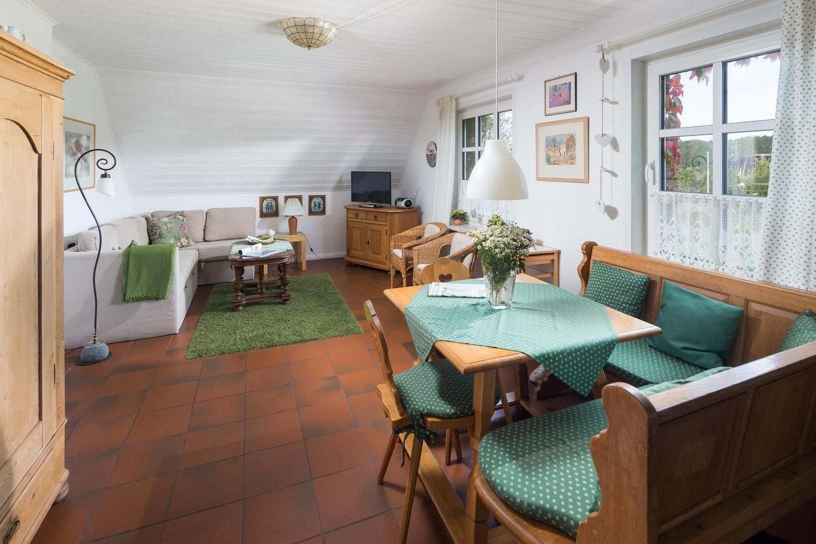 Wohn- und Essbereich mit Holzmöbeln, grüner Tischdecke und Terrakottaboden.