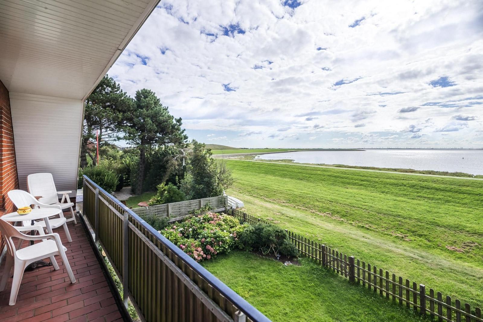 Terrasse mit Sitzgelegenheiten und Blick auf Grünfläche und Wasser.