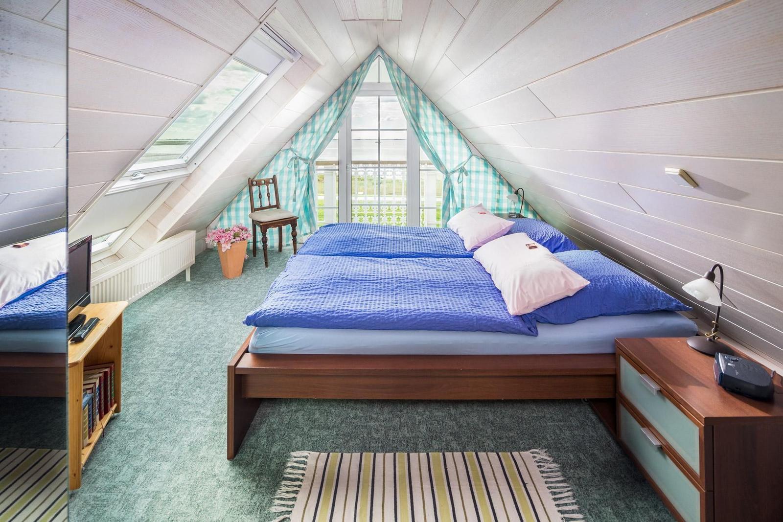 Schlafzimmer mit Dachfenster, Balkon und Bett mit blauer Bettwäsche.