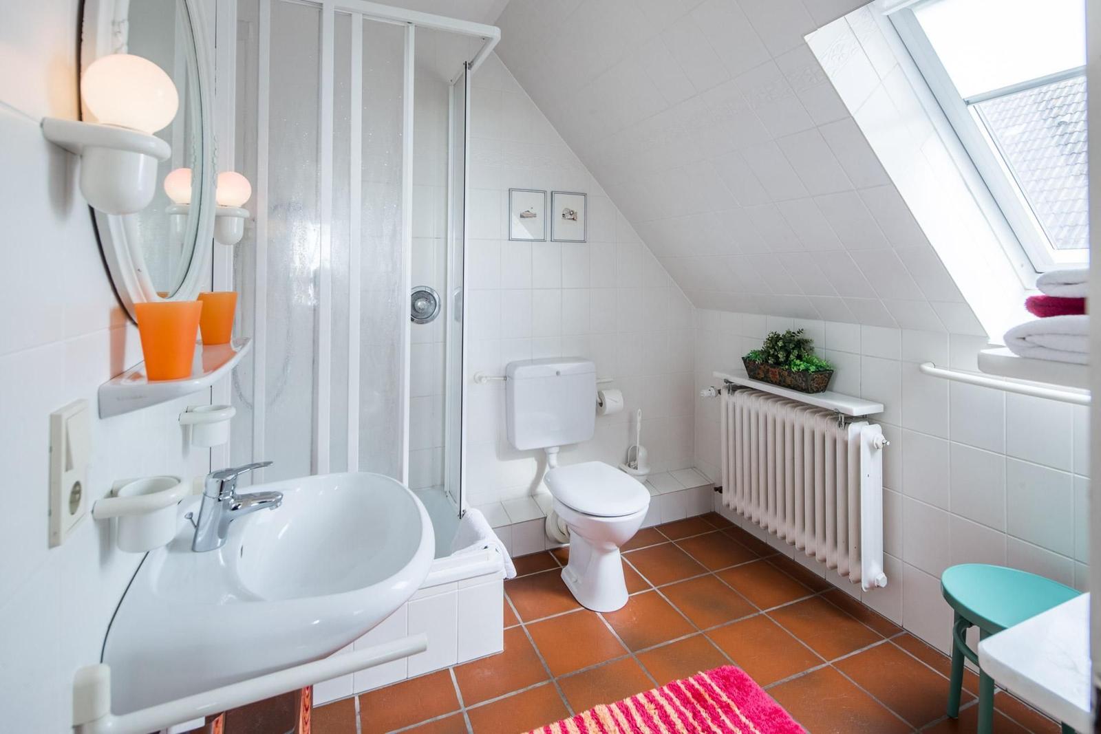 Badezimmer mit Dusche, Toilette, Waschbecken und Dachfenster.