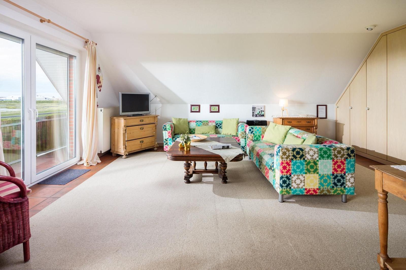 Wohnzimmer mit Sofa, Couchtisch und TV. Terrasse mit Blick nach draußen.