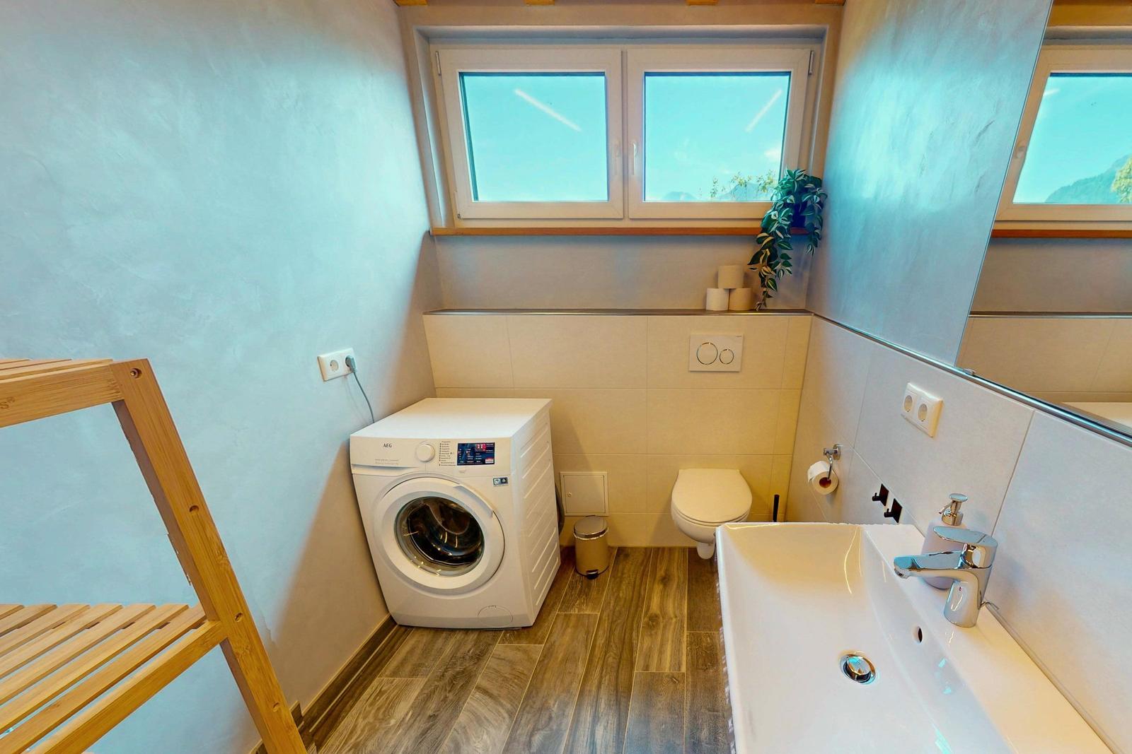 Badezimmer mit Waschmaschine, WC und Waschbecken. Holzfußboden und Fenster mit Blick.