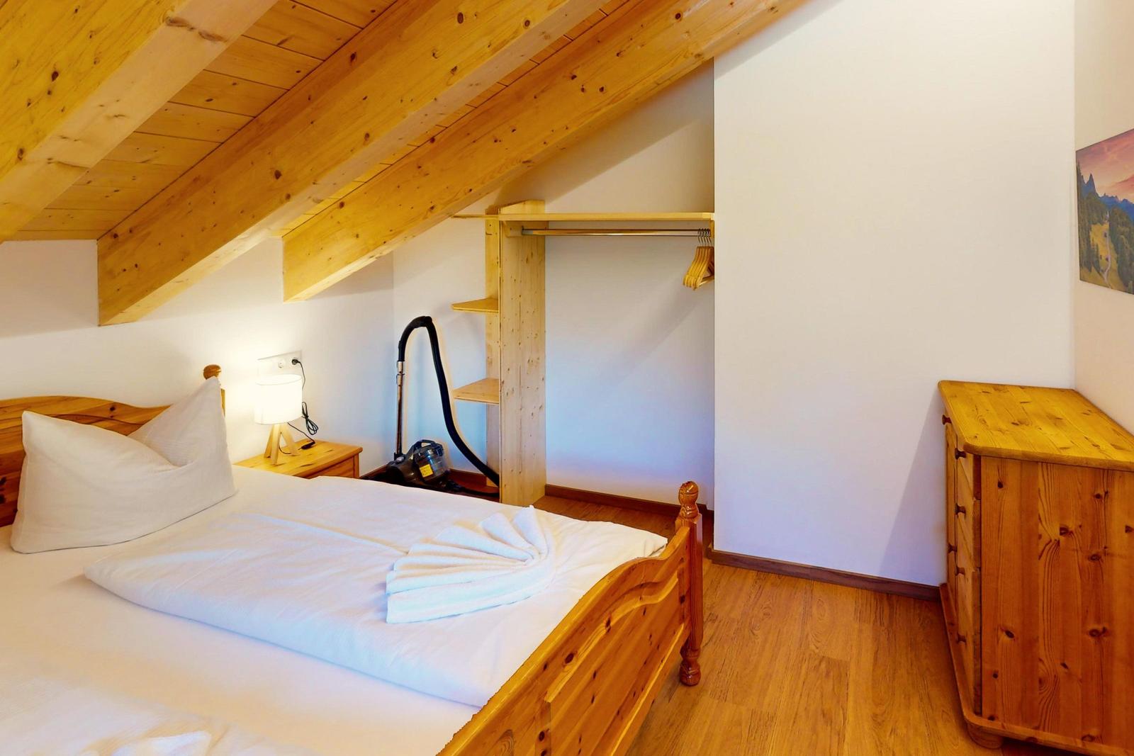 Schlafzimmer mit Holzbett, Kleiderschrank und Dachschrägen.