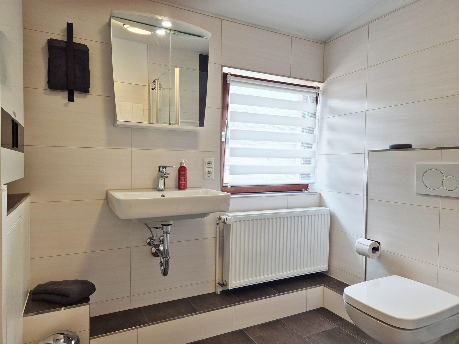 Bathroom with sink, mirror, toilet, and window with blinds.