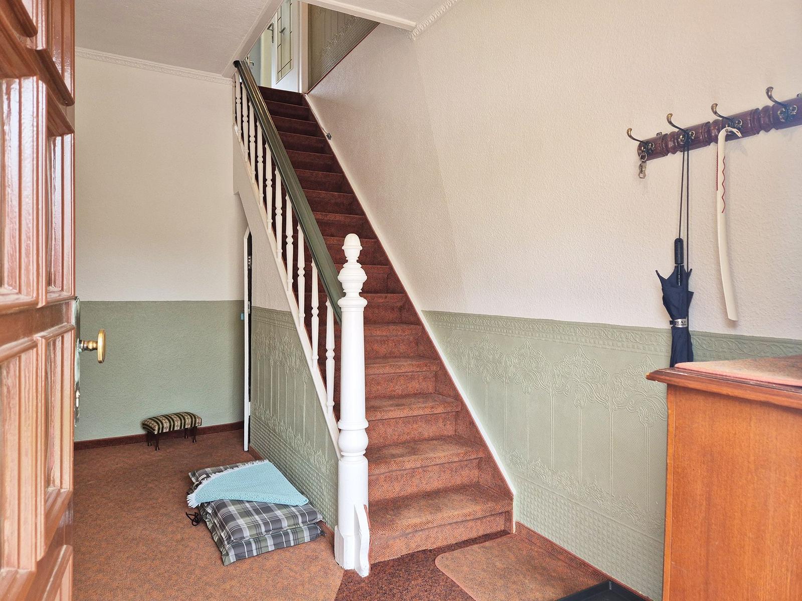 Staircase with wooden steps, wall paneling, and coat rack with umbrellas.
