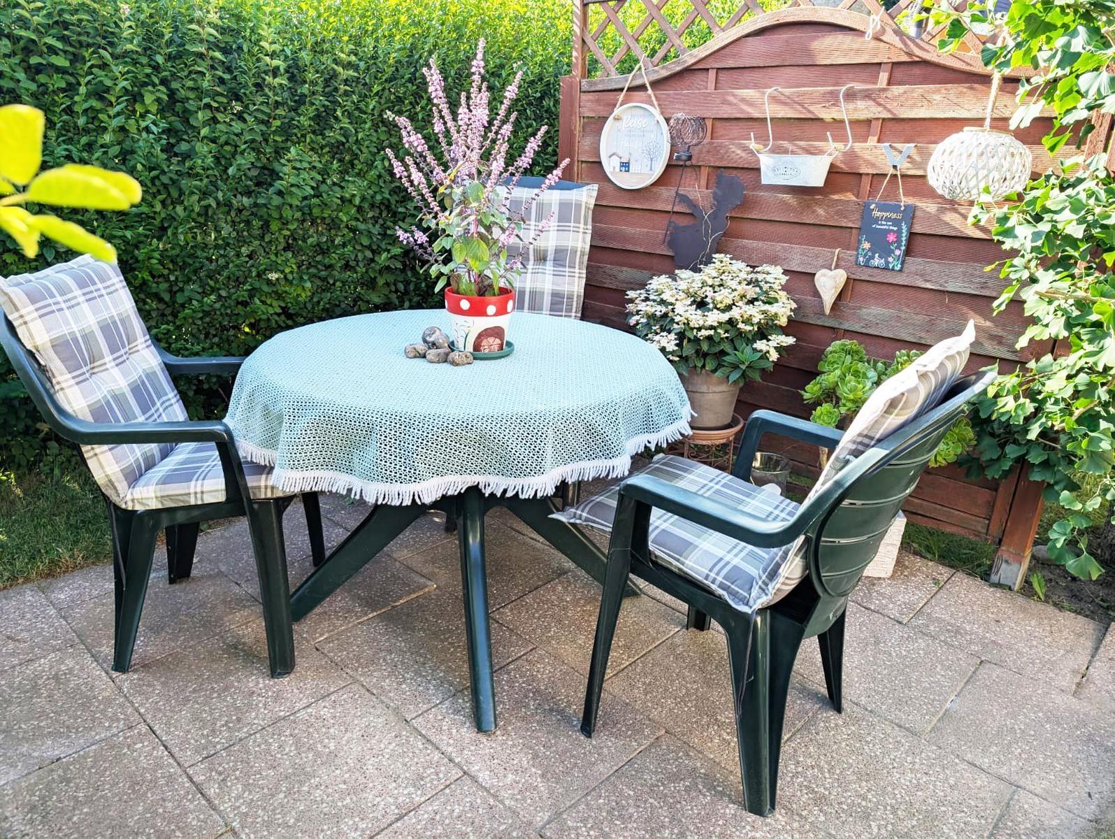 Round table with chairs, tablecloth, and plants in the garden.