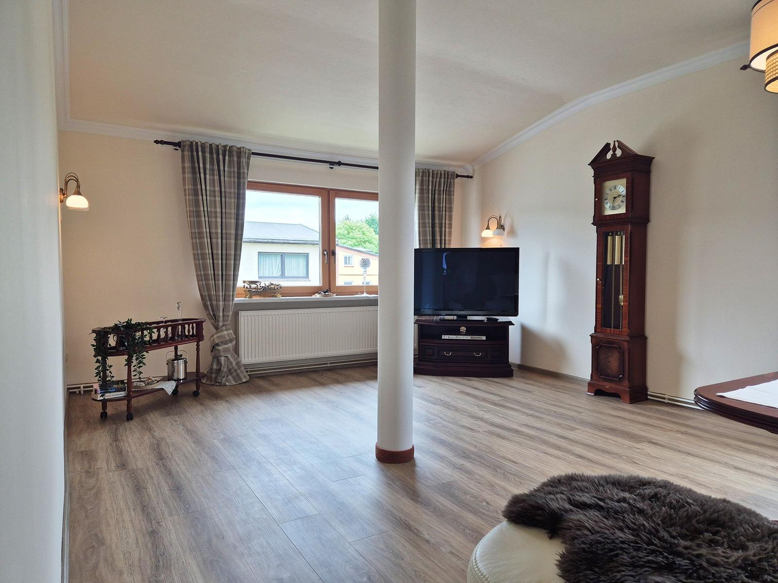 Living room with wooden floor, TV, grandfather clock, and window view.